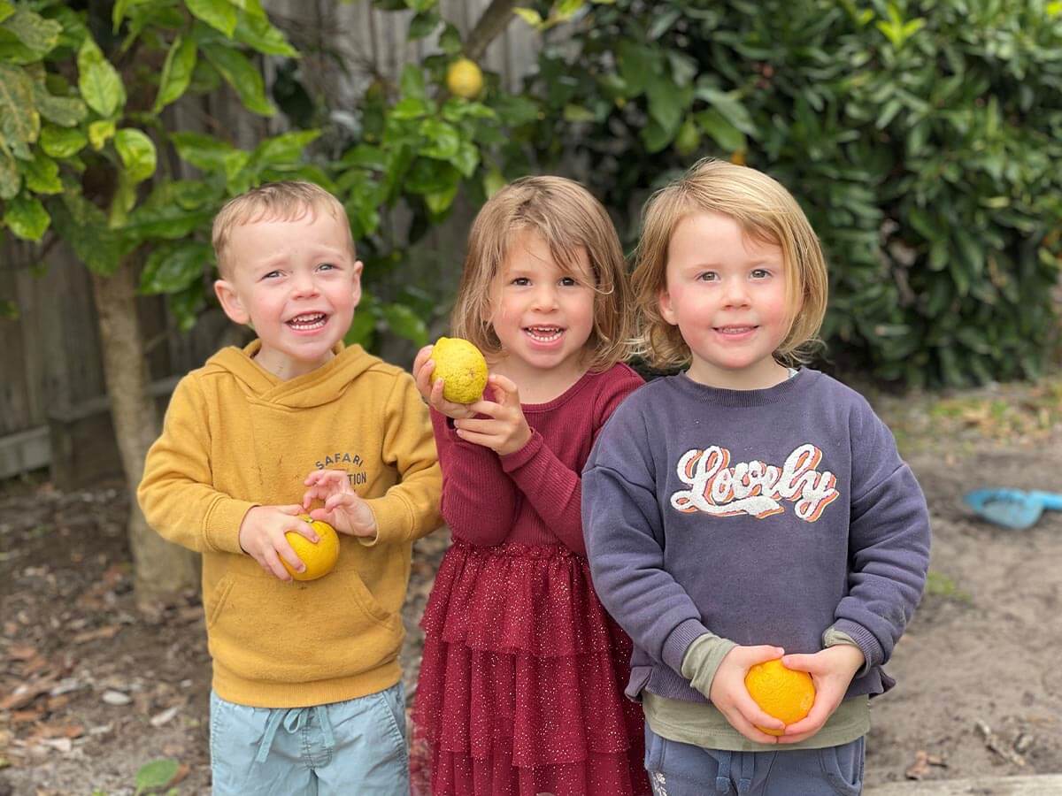 Three small children in our children's centre garden holding home-grown produce